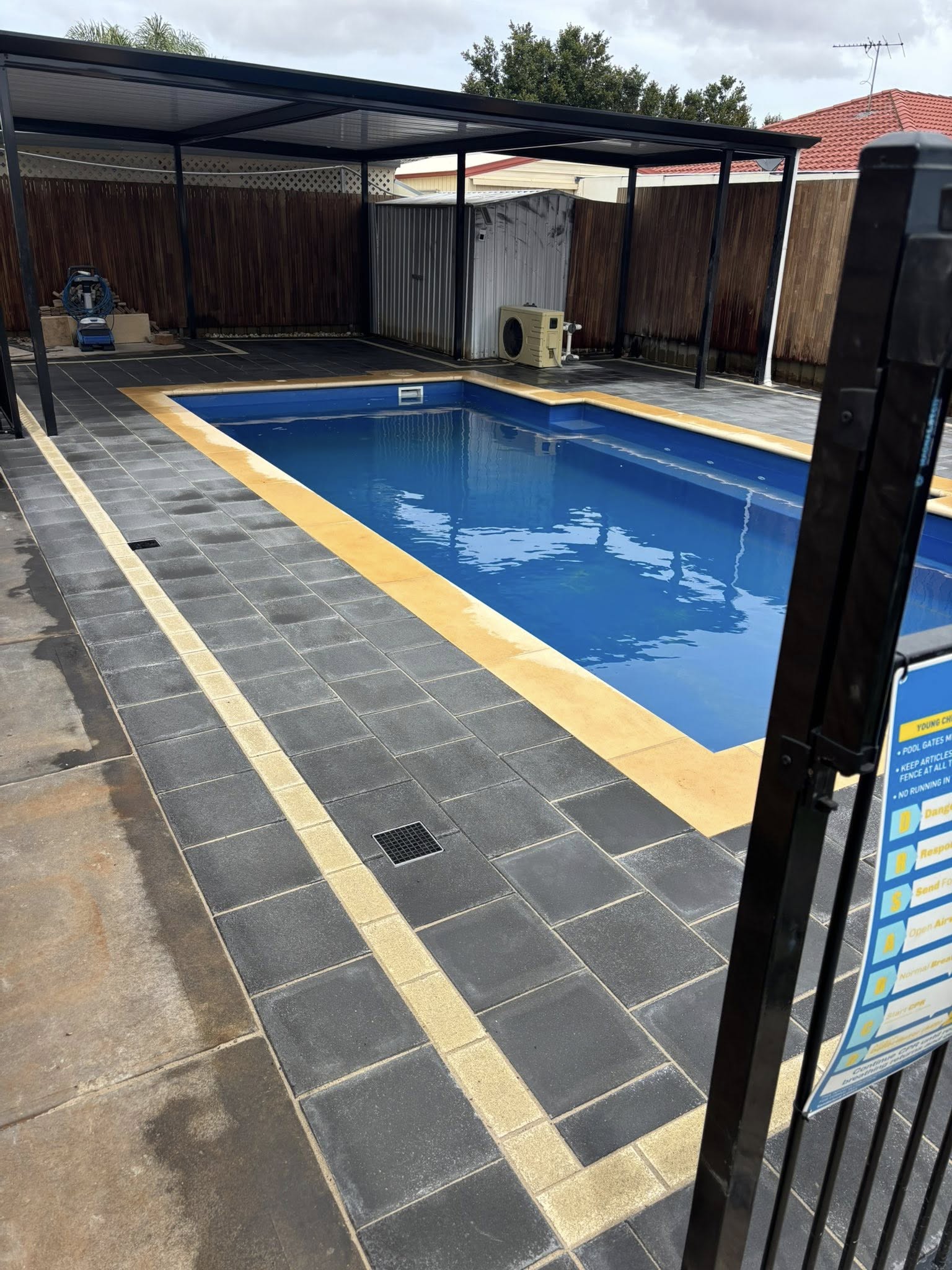 The same pool finished — full wet-look charcoal paver surround with gold sandstone contrast — May Paving