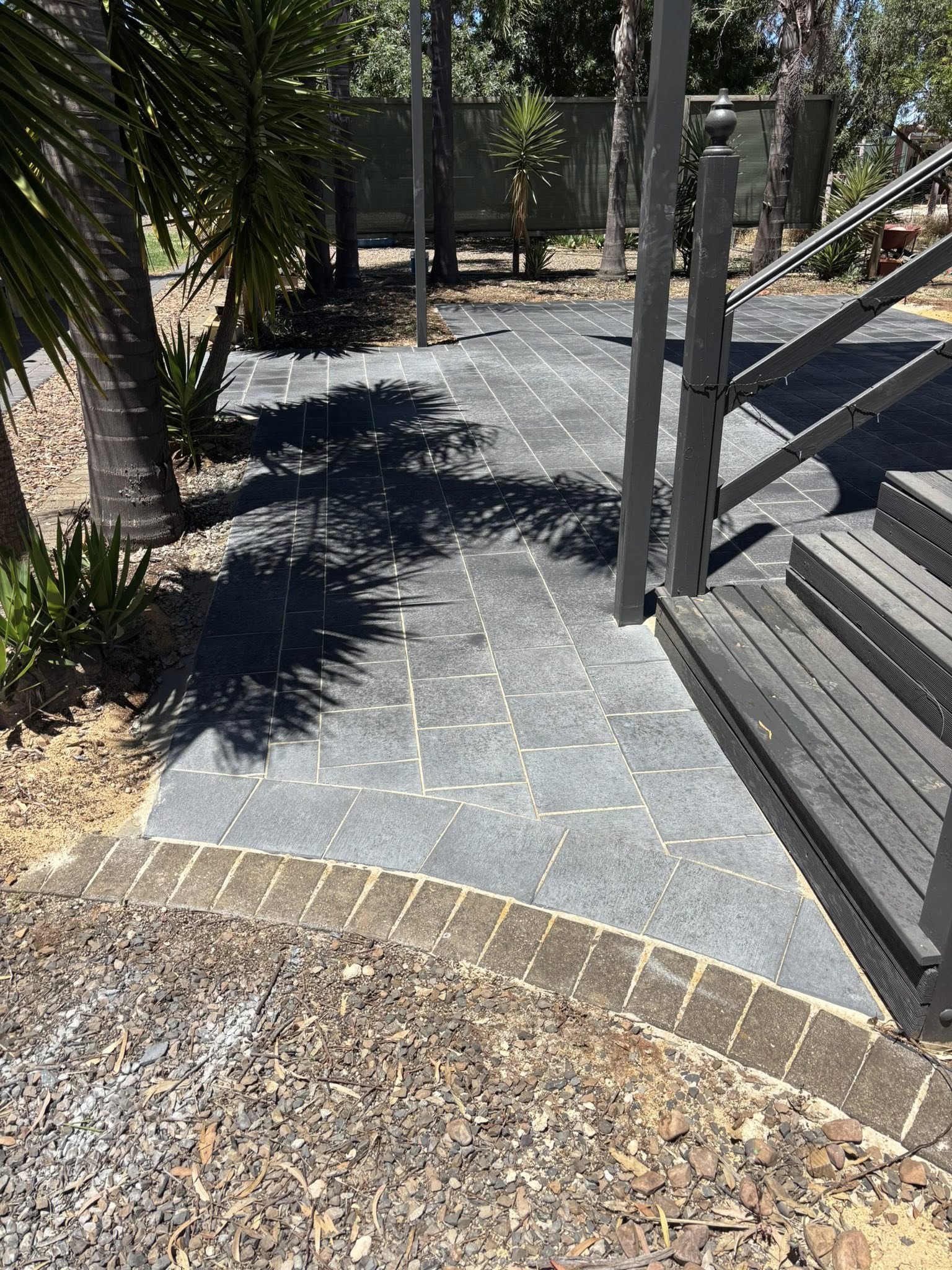 Diagonal-laid charcoal paving with brick soldier edge meeting black composite steps — May Paving