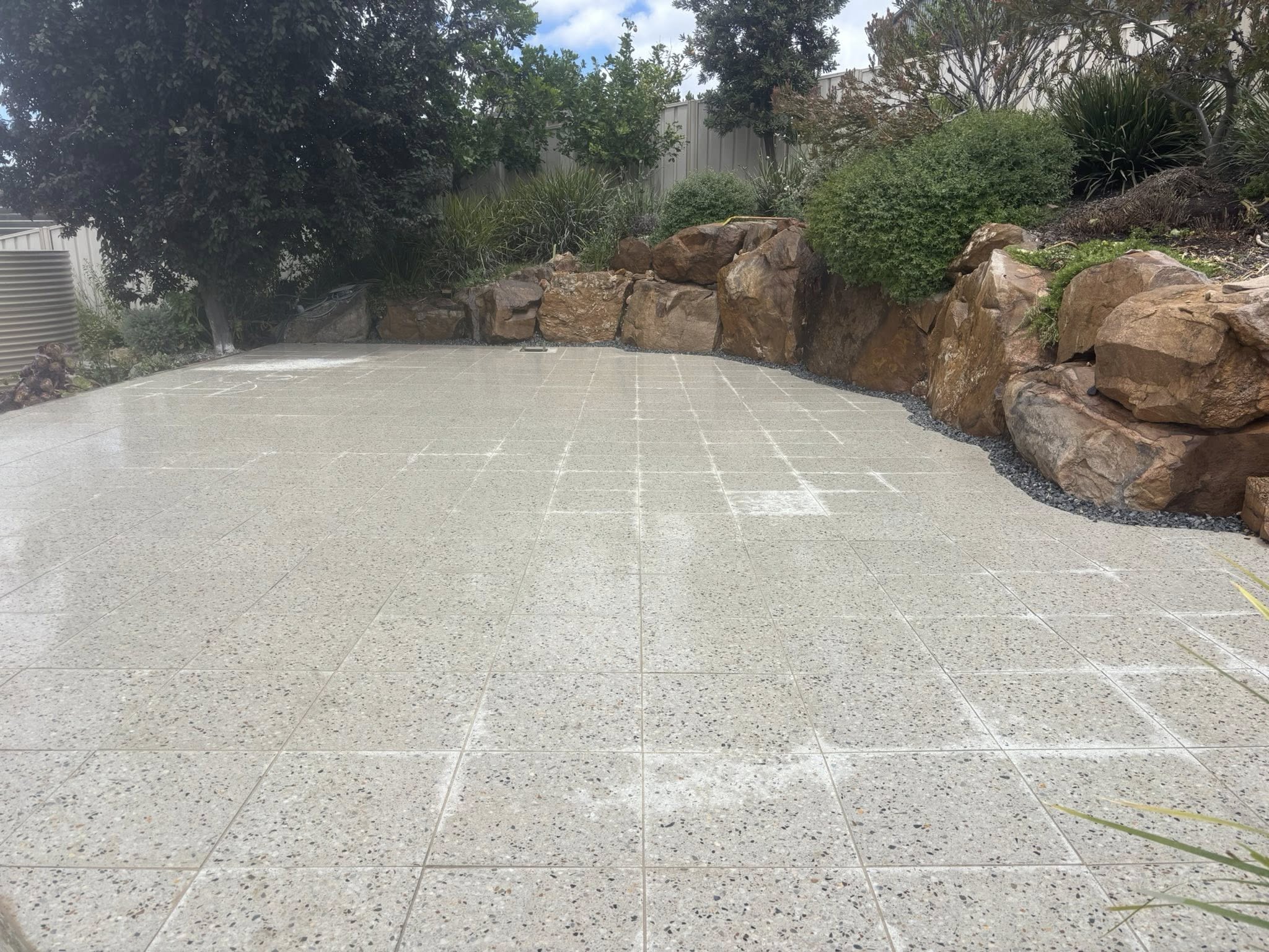 Granite speckled patio with boulder retaining wall and garden landscaping