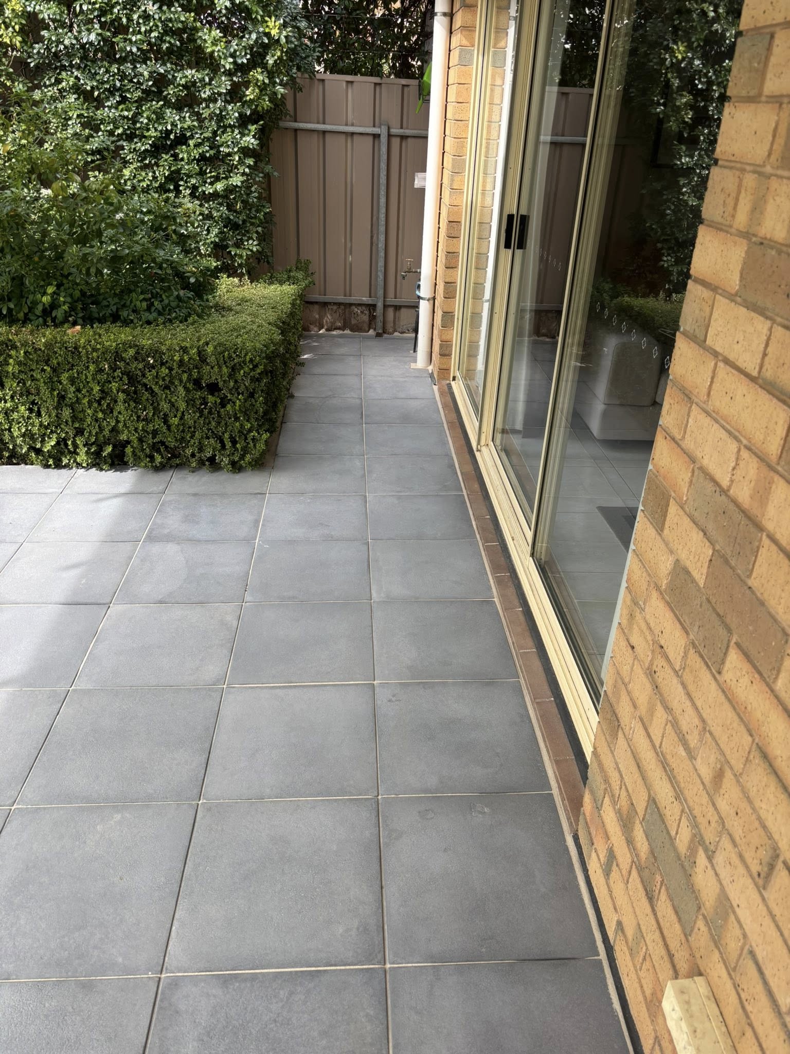 Grey large format tile patio under pergola — covered outdoor entertaining area with hedge garden