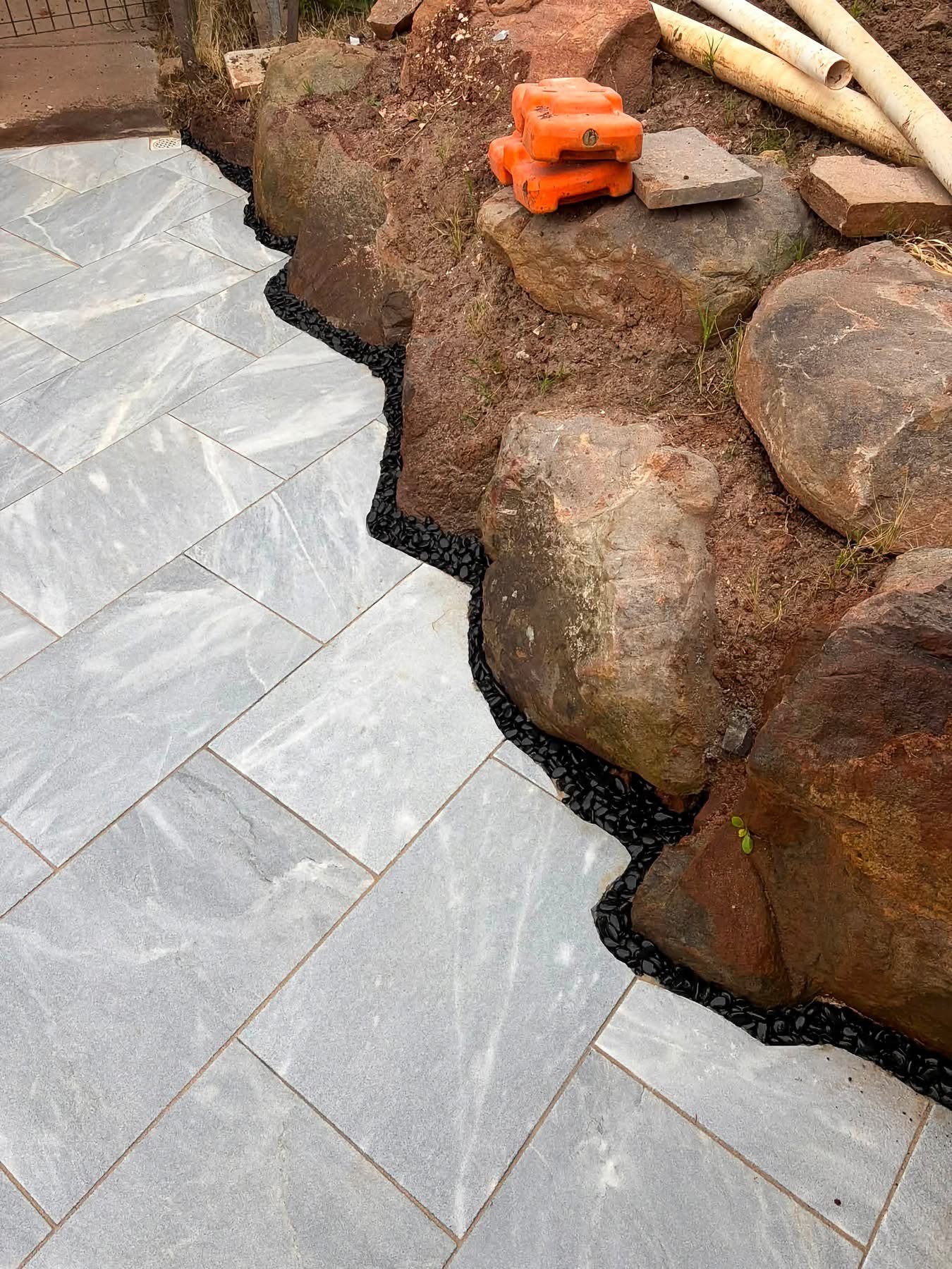 Marble-look pavers scribed by hand around natural boulders with a black pebble border — May Paving detail work