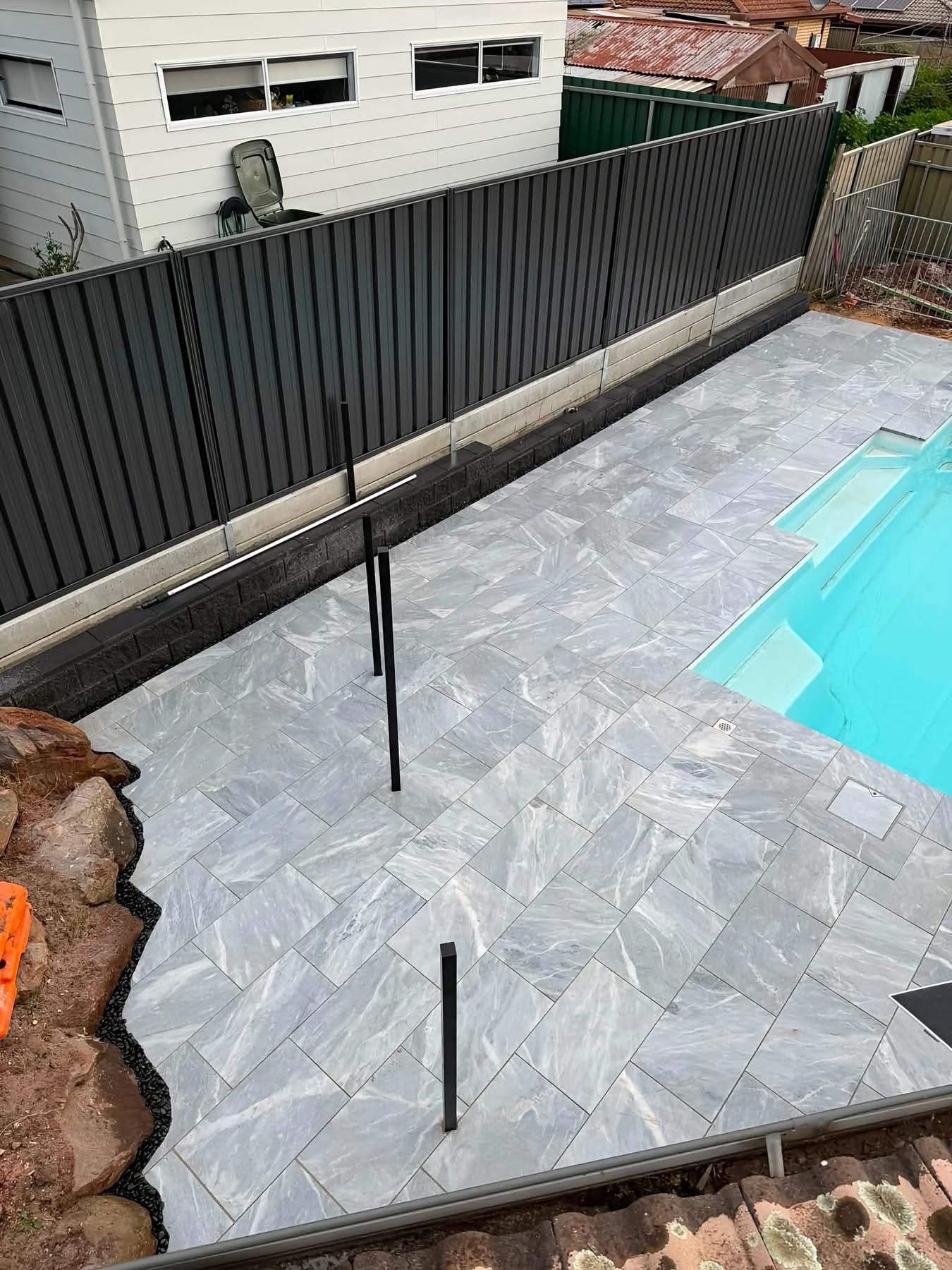 Long run of marble-look paving along a dark fence line and block retaining wall — May Paving