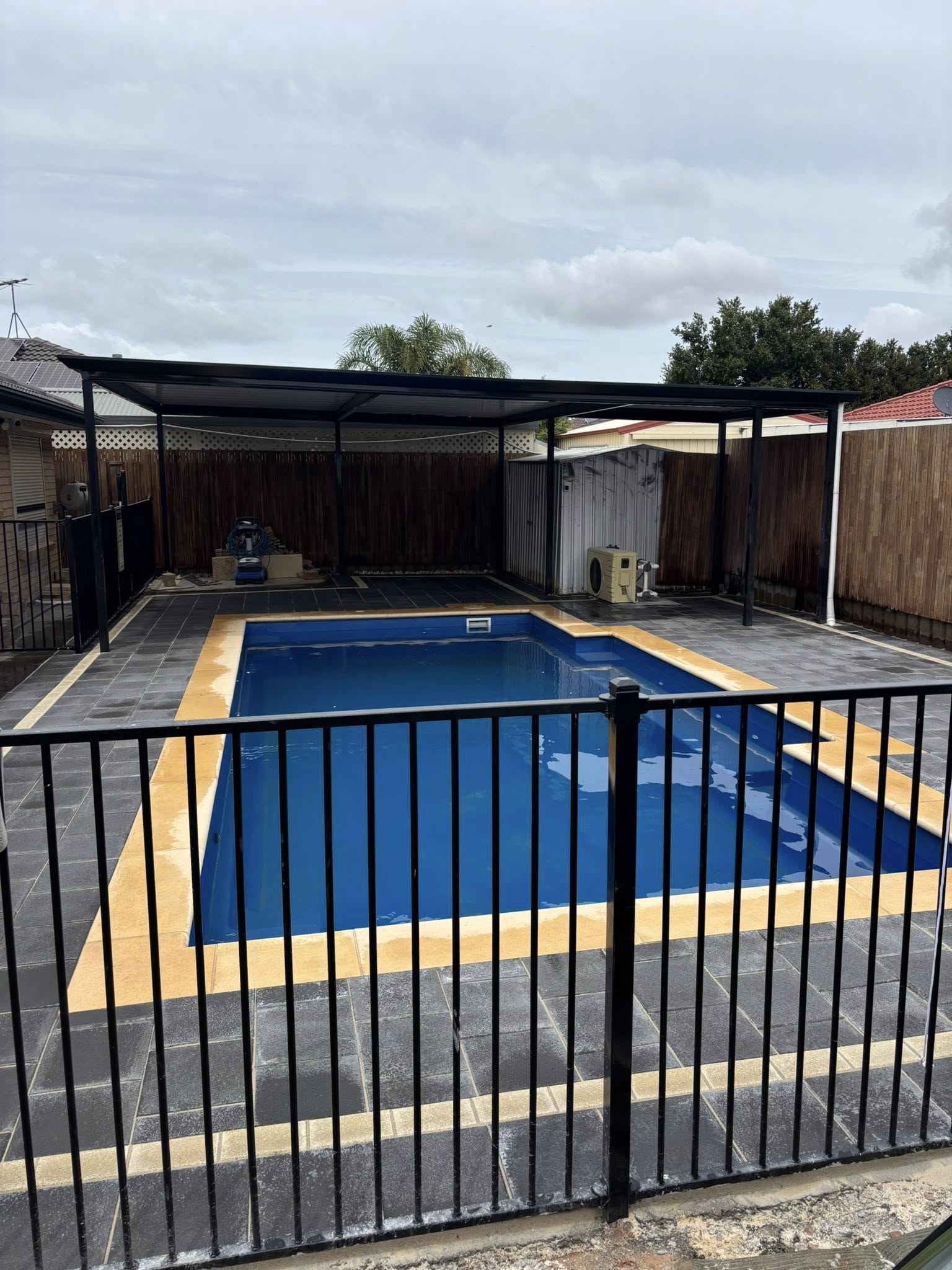 Completed pool surround — dark slate tiles with gold border, black pool fence