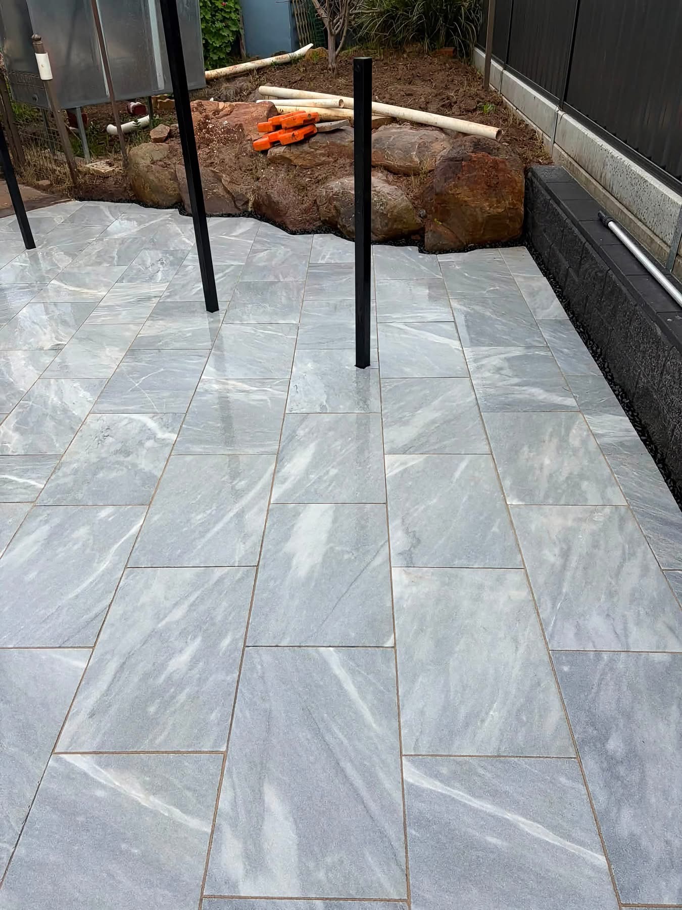 Clean field of marble-look pavers running to a charcoal block retaining wall — May Paving pool surround