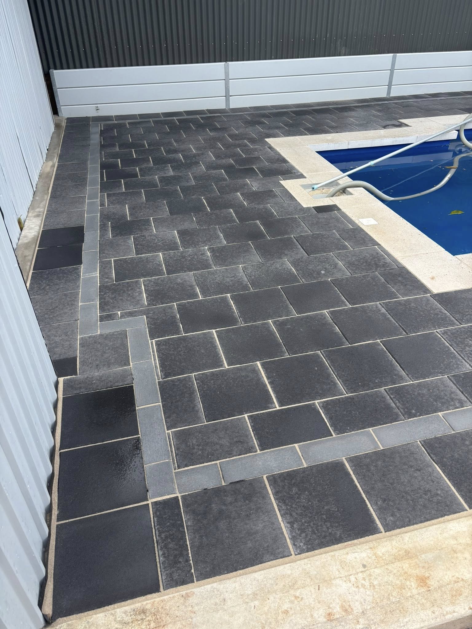 Pool surround close-up — charcoal slate tiles with gold sandstone coping