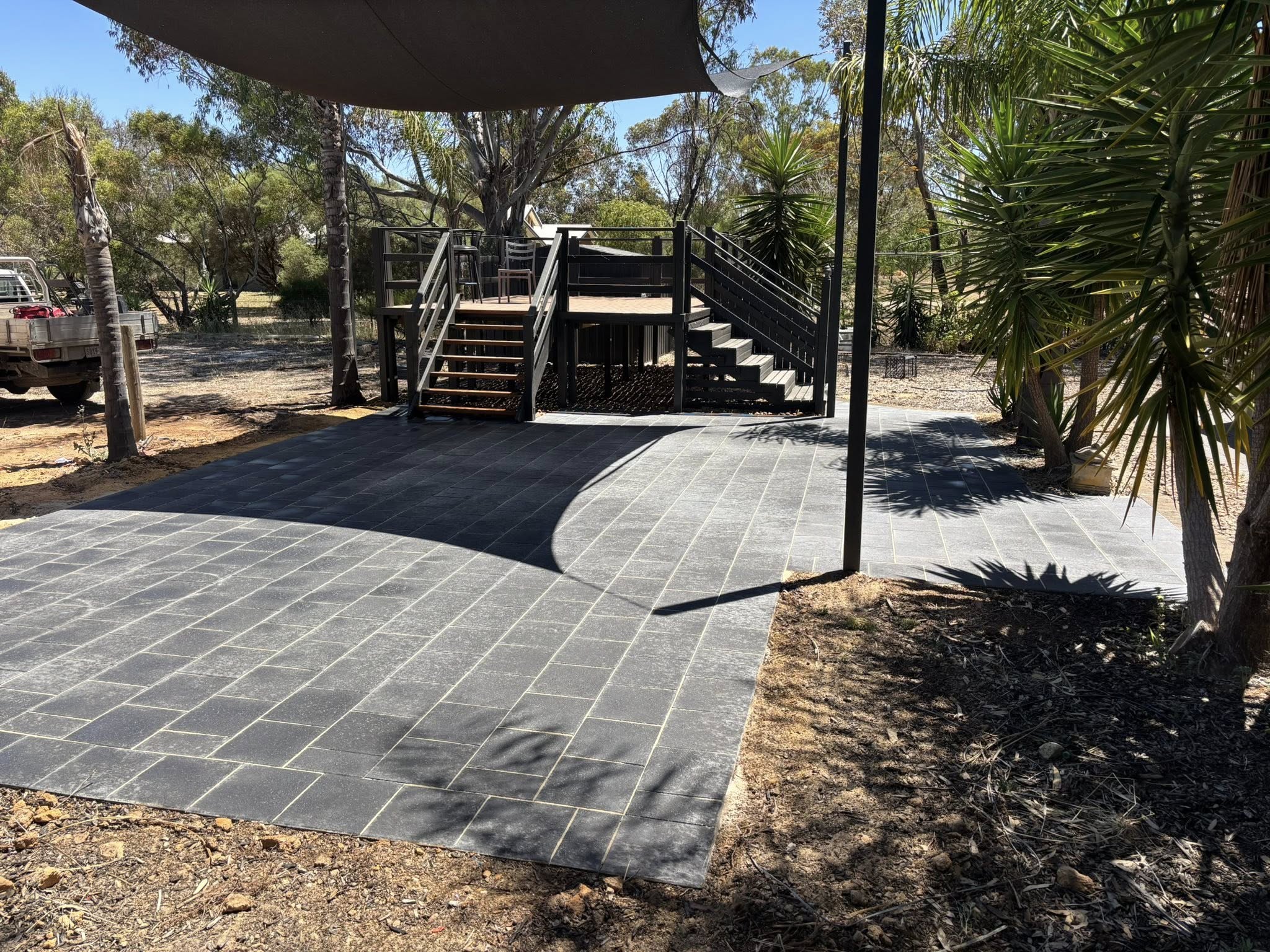 Wide dark slate patio under shade sail with composite deck and staircase