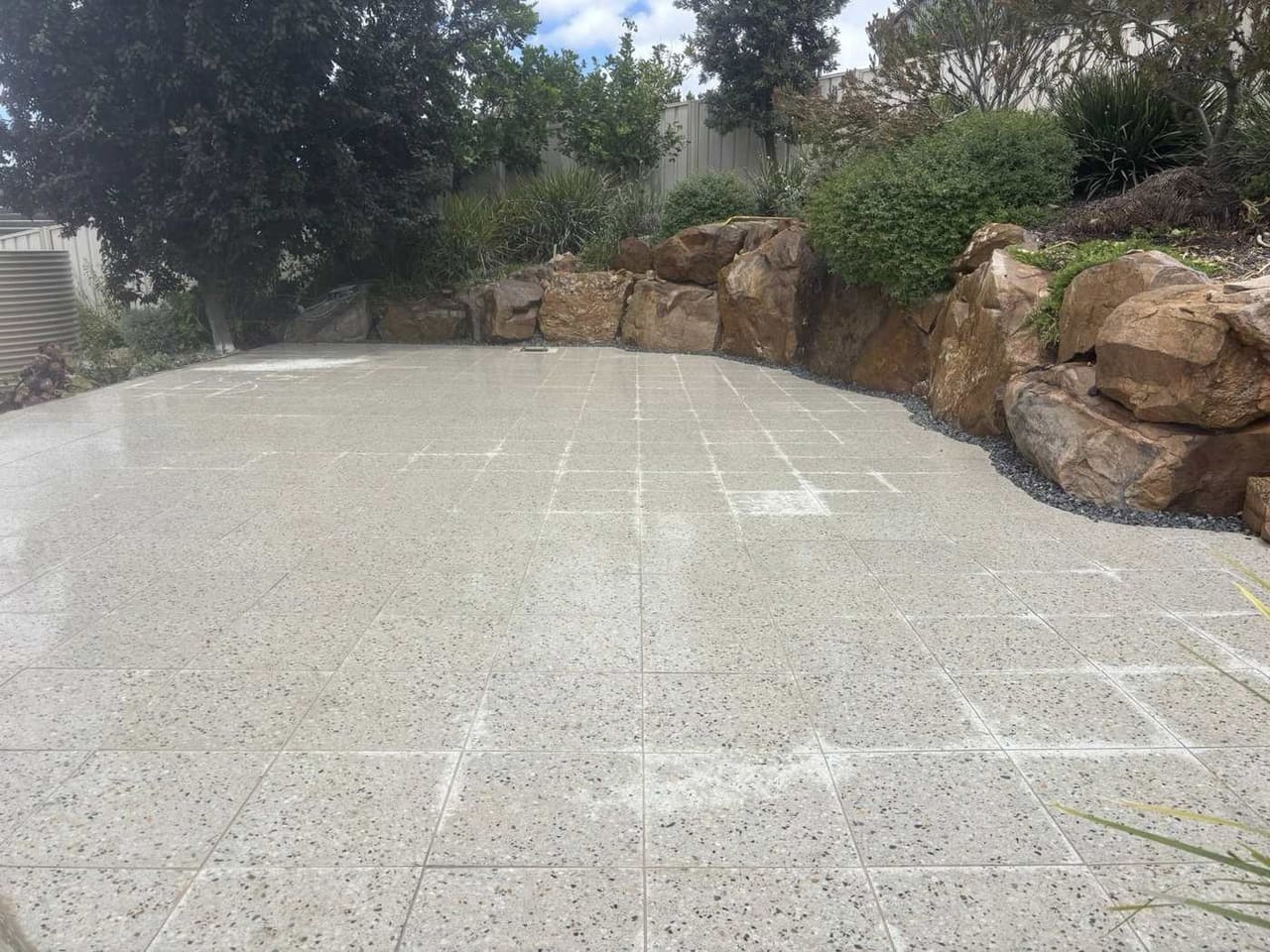 Natural boulder retaining wall holding a garden bed above a speckled granite patio