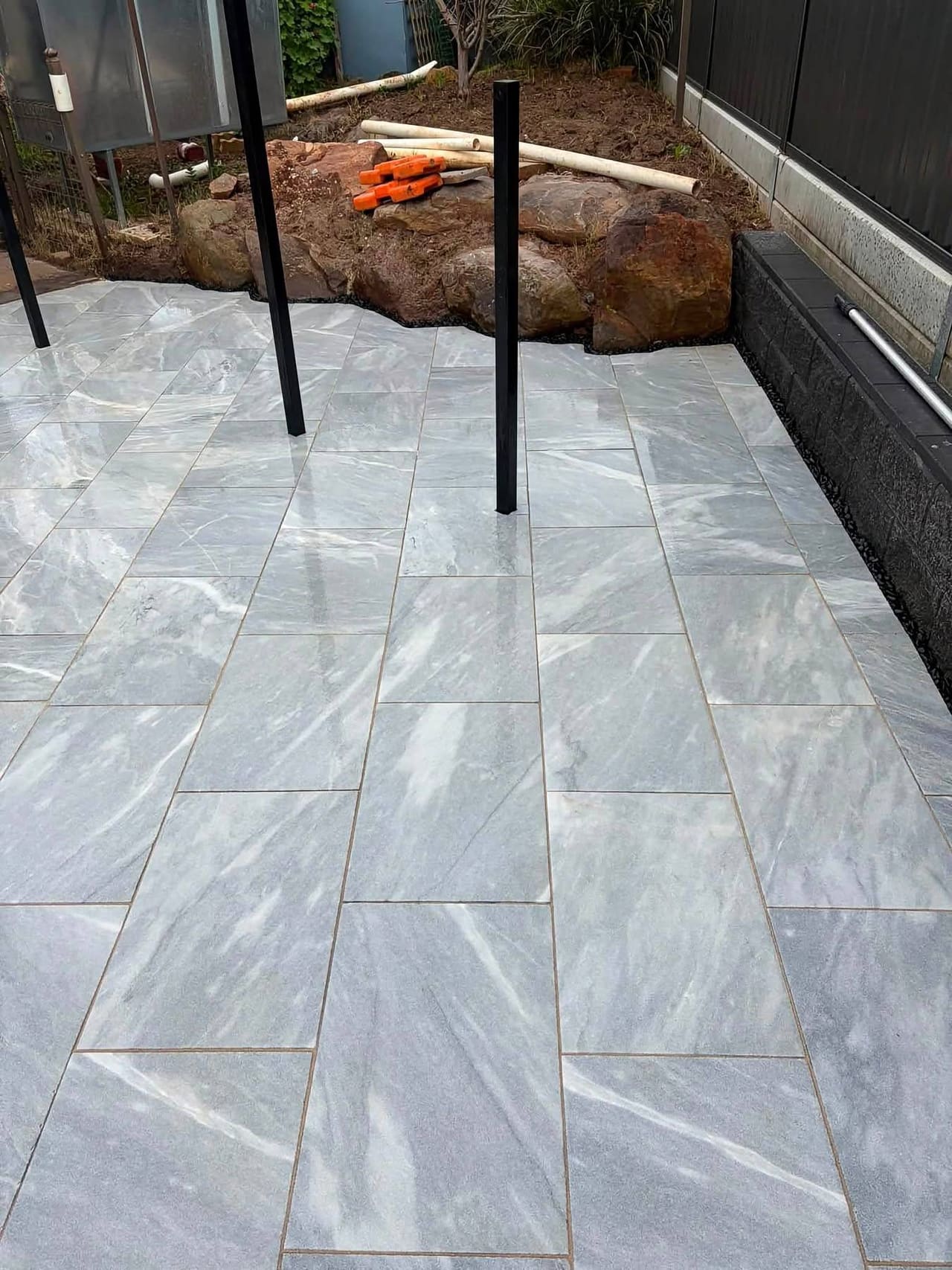 Clean field of marble-look pavers running to a charcoal block retaining wall — May Paving